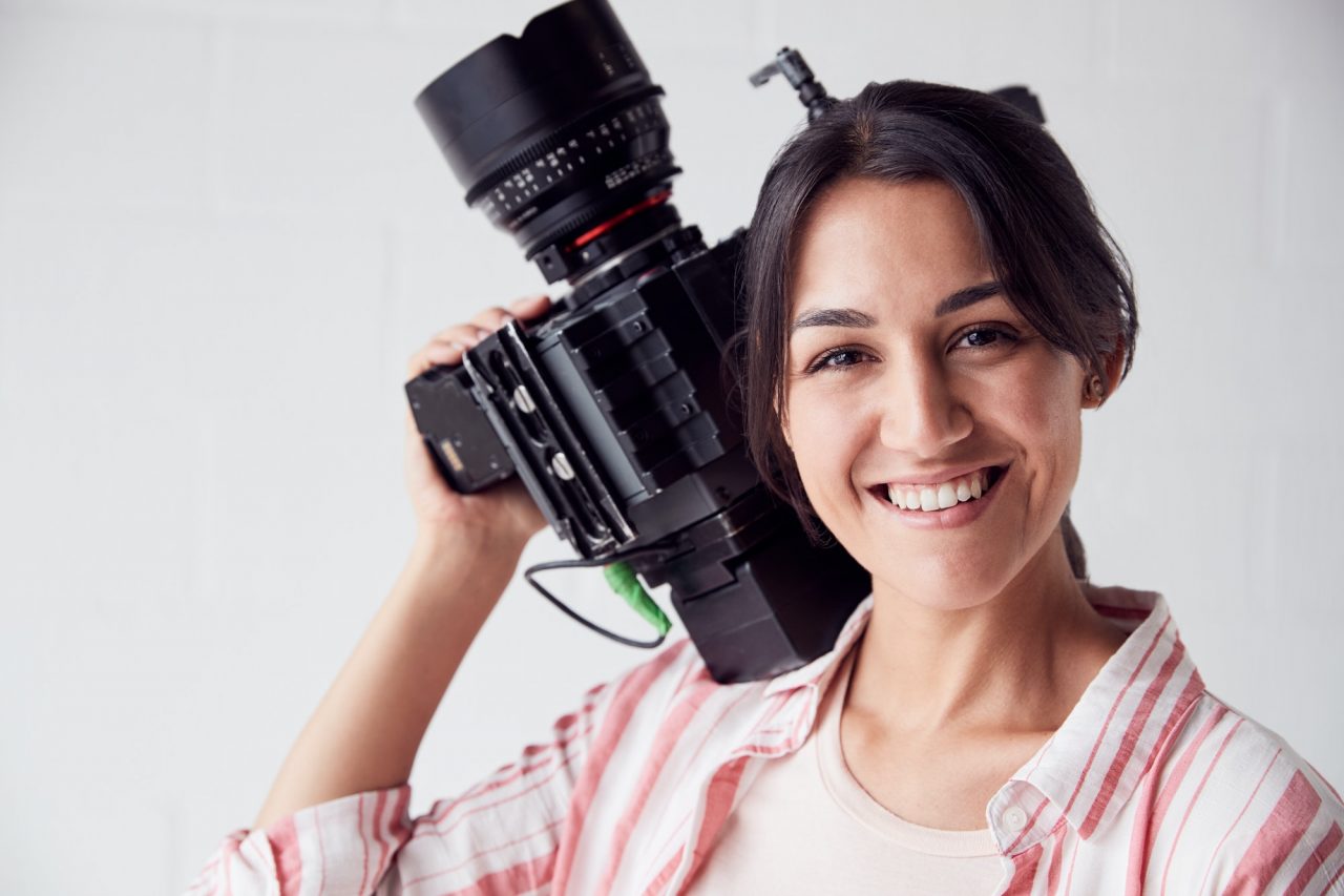 Portrait of female videographer with video camera filming movie in white studio.jpg | ProMedia