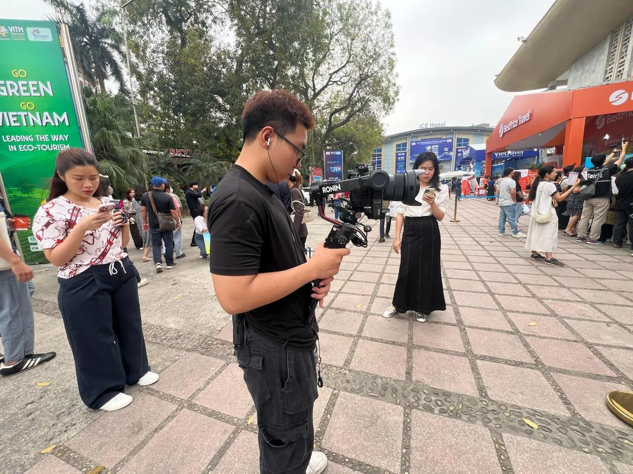 Cameraman ProMedia đang sử dụng gimbal Ronin để ghi hình, phía sau là gian hàng BestPrice Travel và Vietnam Airlines tại triển lãm.