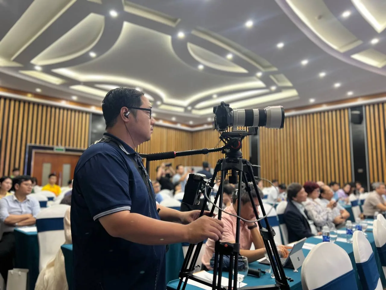 Quay phim viên ProMedia với máy ảnh chuyên nghiệp tại hội trường.