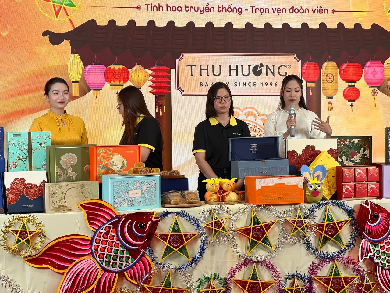 Người giới thiệu và các hộp bánh trung thu được chiếu sáng rõ nét trên sân khấu.